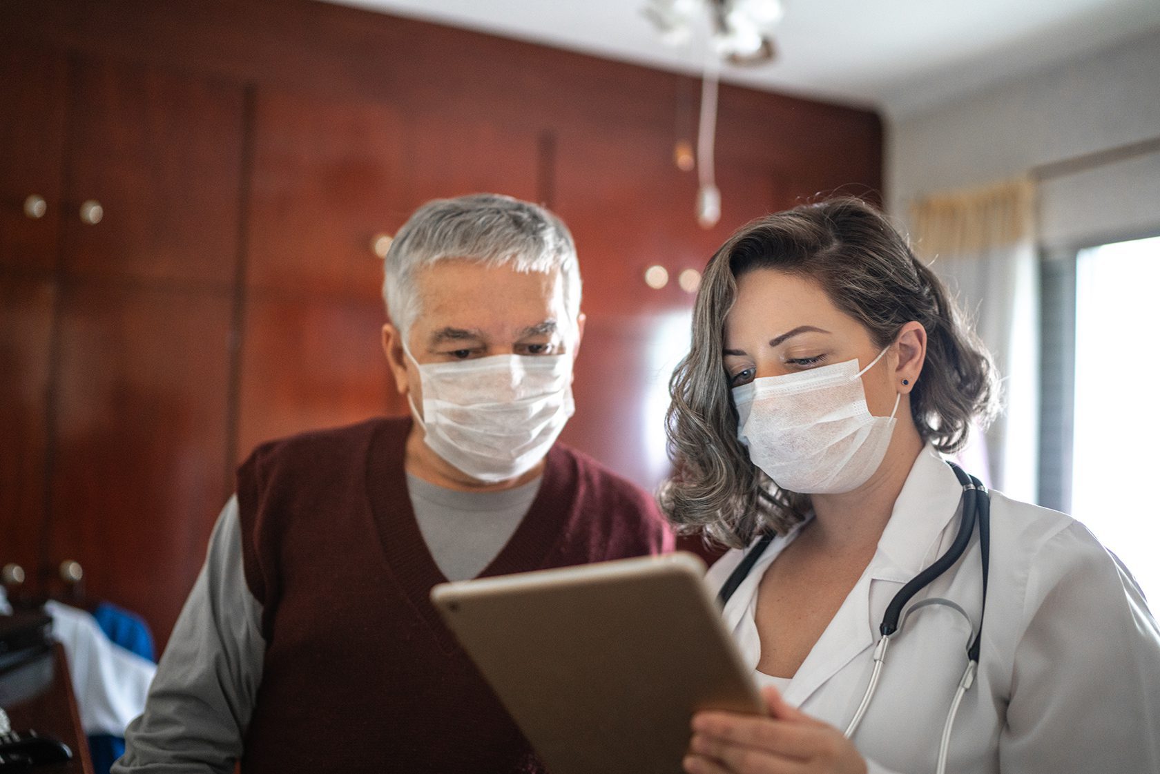 doctor and patient reviewing tablet while wearing masks.