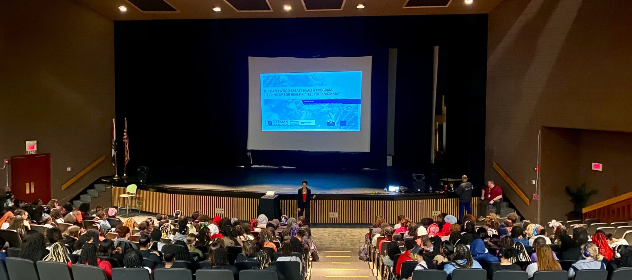 Doctor Lannis Hall presents breast health information on screen in large auditorium