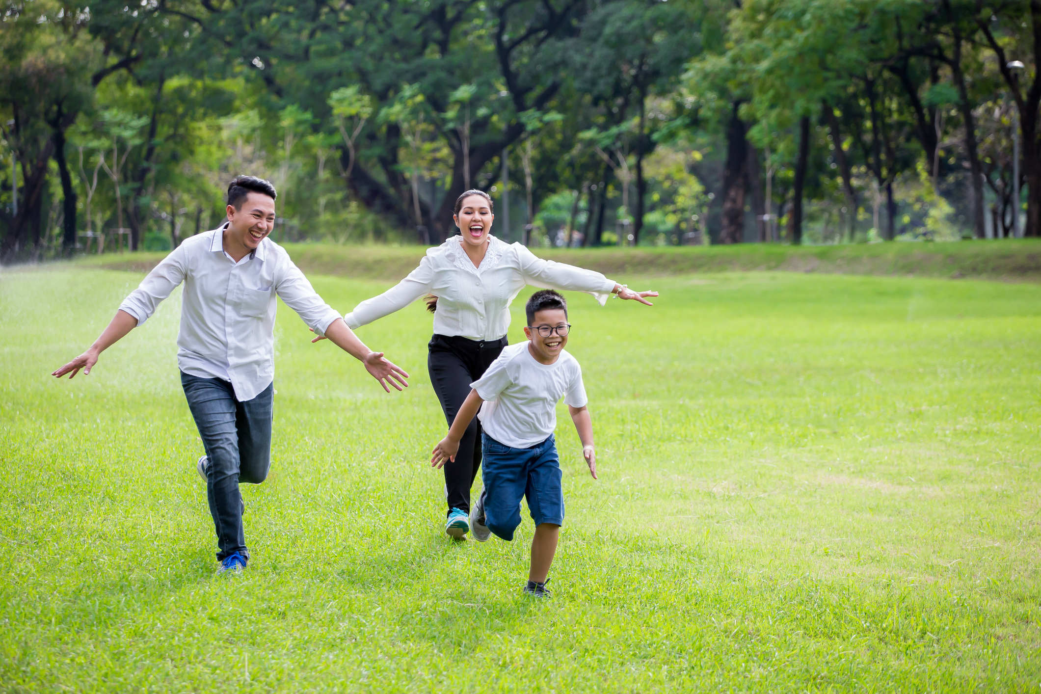 Happy Parents And Their Children Running Around In Park Together.