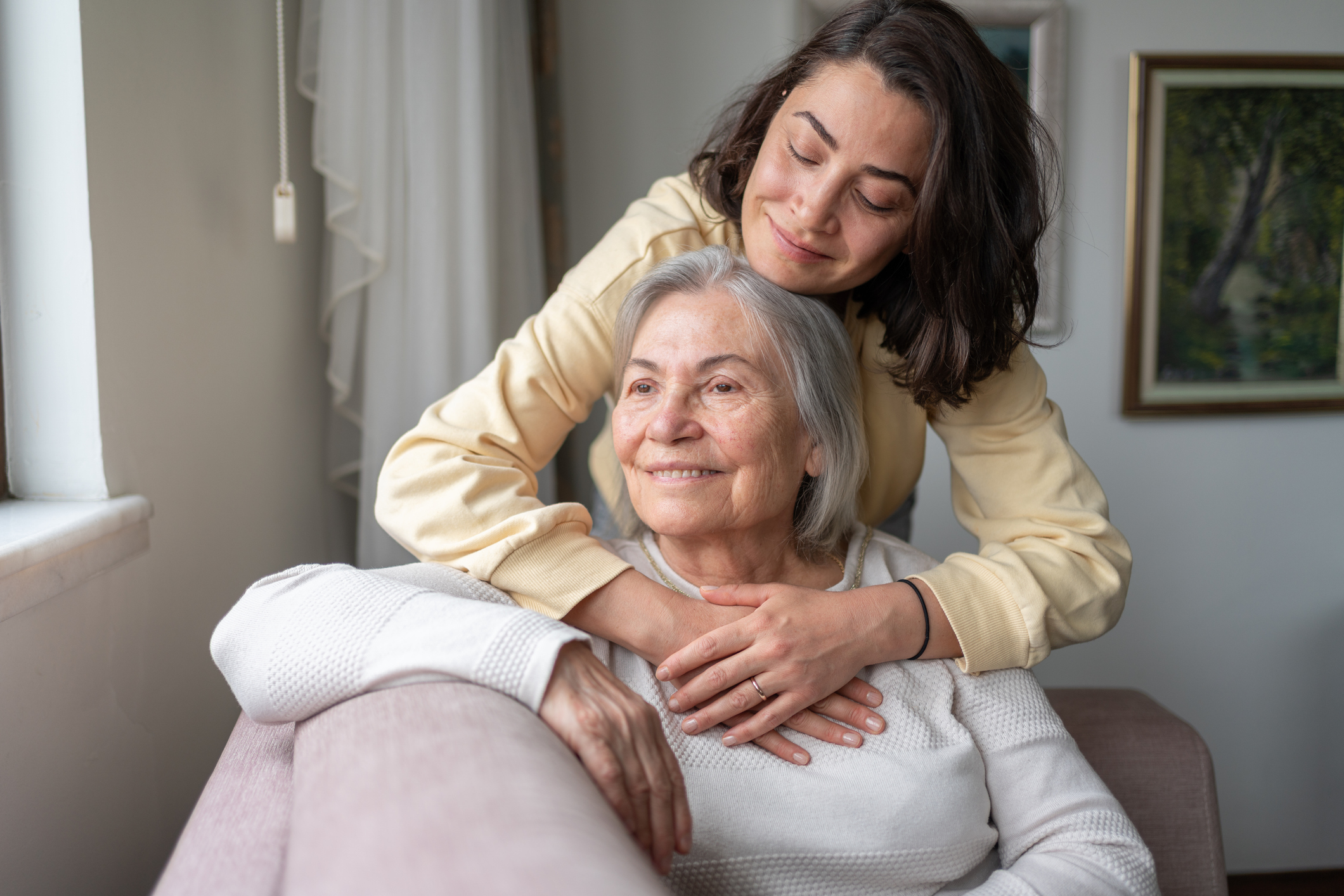 Daughter Hugging Senior Mother From Behind Holding Hands